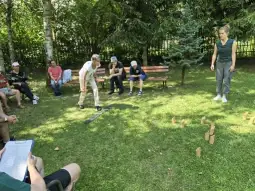 Dzieci grają w grę na świeżym powietrzu, a dorośli obserwują z ławki.