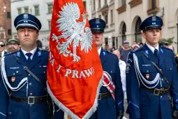 Trzej mężczyźni w mundurach trzymają flagę z orłem białym.