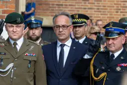 Mężczyzna w garniturze otoczony przez funkcjonariuszy służb mundurowych.
