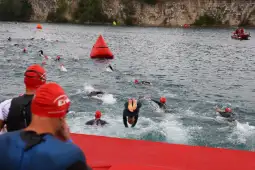 Zawodnicy w strojach pływackich skaczą do wody podczas wyścigu triathlonowego.