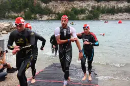 Zawodnicy w strojach triathlonowych wychodzą z wody po etapie pływackim.
