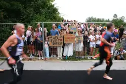Grupa kibiców trzymająca transparenty, wspierająca uczestników wyścigu triathlonowego.