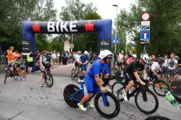 Zawodnicy na rowerach przejeżdżają przez bramę startową wyścigu rowerowego.