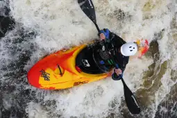 Kajakarz pokonujący wzburzone wody w pomarańczowym kajaku.