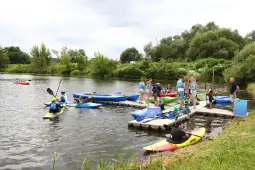 Grupa osób pływających na kajakach i przygotowujących się do wyprawy nad wodą.