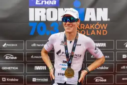 Zawodnik triathlonowy z medalem na tle banera Ironman 70.3 w Krakowie.