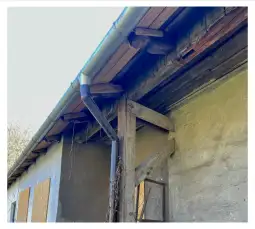 Zniszczona elewacja budynku z drewnianymi elementami i rynną.