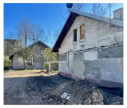 Dwa budynki mieszkalne w trakcie remontu, z widocznymi pracami ziemnymi i drzewami w tle.