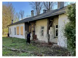 Zniszczony budynek z zasłoniętymi oknami i osobą sprzątającą teren.
