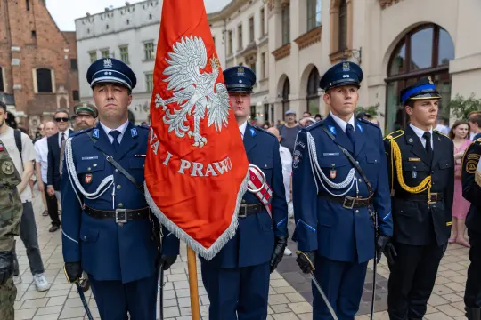 Czterech mężczyzn w mundurach, trzymających flagę z orłem, podczas uroczystości.
