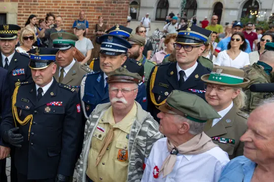 Grupa mężczyzn i kobiet w mundurach wojskowych i policyjnych, uczestniczących w wydarzeniu publicznym.