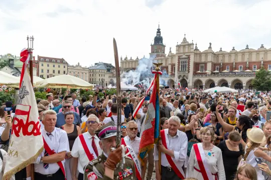 Tłum ludzi z flagami i sztandarami na rynku w Krakowie, z widoczną architekturą w tle.