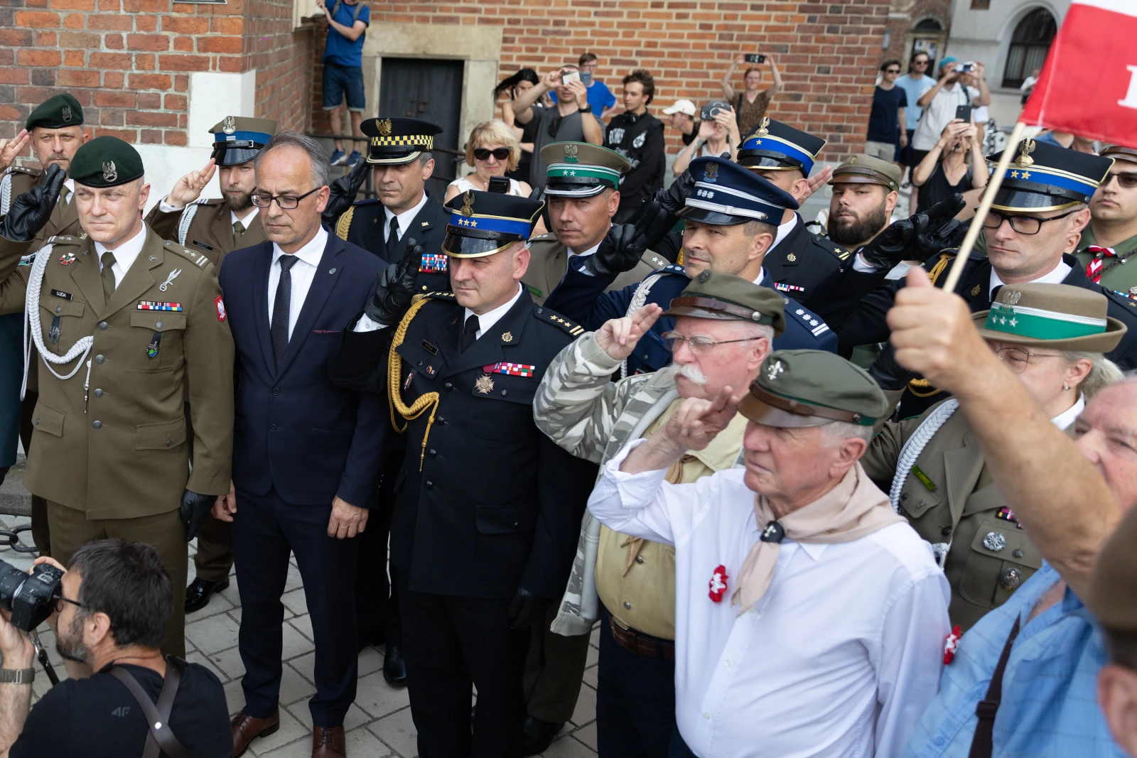 Grupa mężczyzn w mundurach i cywilnych strojach, salutujących podczas uroczystości.  Autor: Bogusław Świerzowski