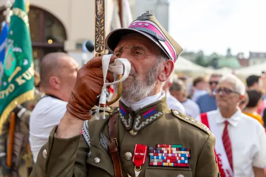 Mężczyzna w mundurze wojskowym z medalami, grający na trąbce podczas uroczystości.