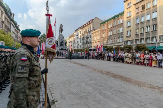 Ceremonia z udziałem żołnierzy, flagi i tłum ludzi na ulicy.
