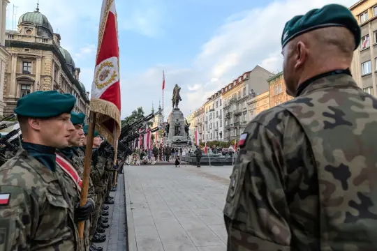 Żołnierze w mundurach wojskowych podczas ceremonii z pomnikiem w tle.