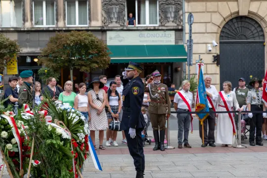 Ceremonia złożenia wieńca przez strażnika w towarzystwie zgromadzonych ludzi.