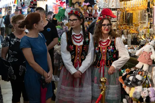 Dwie kobiety w tradycyjnych strojach ludowych, otoczone przez stragany z pamiątkami.