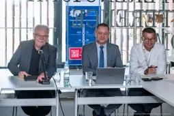 Trzech mężczyzn siedzących przy stole, prowadzących dyskusję w biurze.