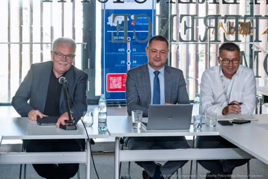 Trzech mężczyzn siedzących przy stole, prowadzących dyskusję w biurze.