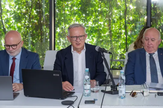 Trzech mężczyzn siedzących przy stole, prowadzących dyskusję w biurze z roślinnością w tle.