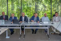 Grupa mężczyzn w garniturach siedzących przy stole w sali konferencyjnej.