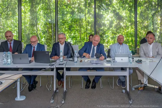 Grupa mężczyzn w garniturach siedzących przy stole w sali konferencyjnej.