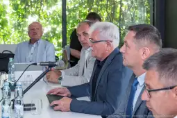 Mężczyźni w garniturach siedzą przy stole, prowadzą dyskusję w otoczeniu zieleni.