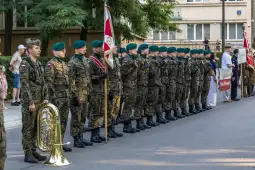 Żołnierze w mundurach wojskowych podczas ceremonii, trzymają flagi i sztandary.