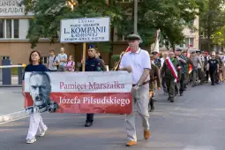Marsz upamiętniający Józefa Piłsudskiego z transparentem i uczestnikami w mundurach.