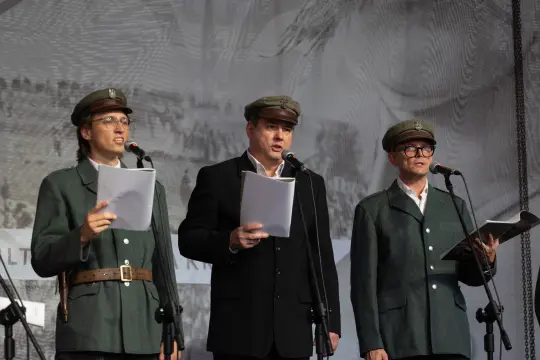 Trzej mężczyźni w mundurach wojskowych recytują teksty na scenie.