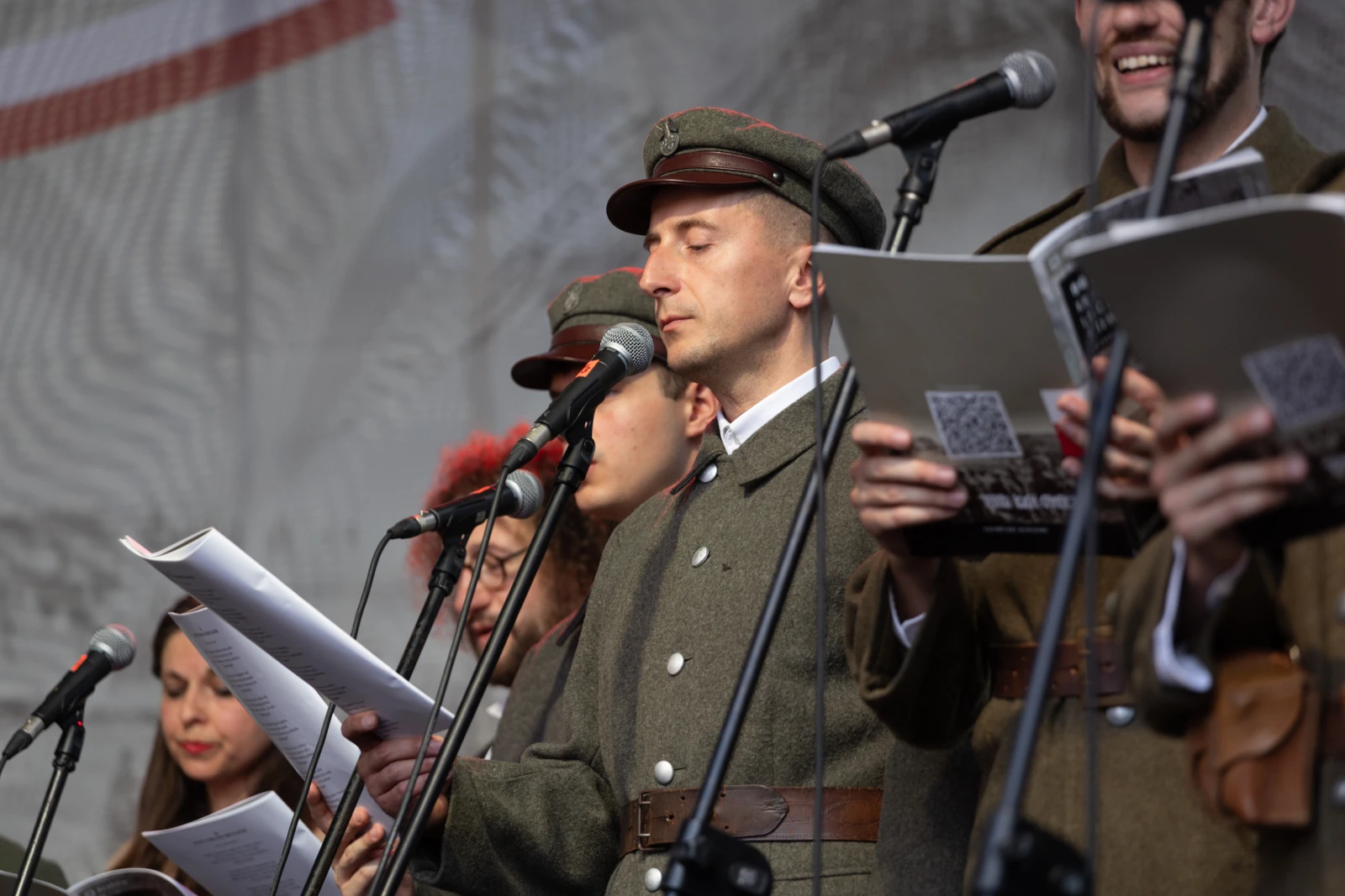 Mężczyzna w mundurze wojskowym recytuje tekst, wokół niego inni wykonawcy z mikrofonami.  Autor: Bogusław Świerzowski