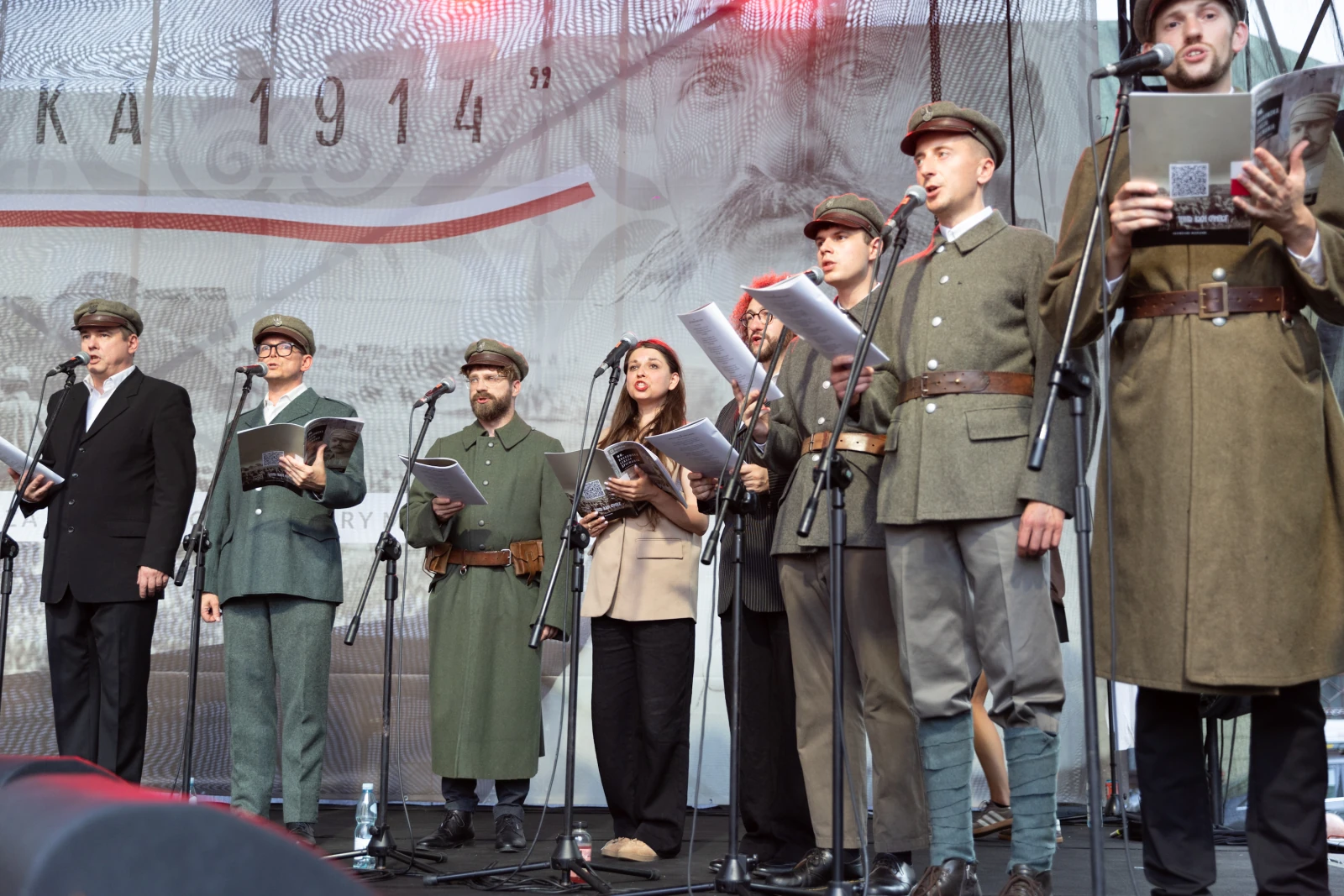 Grupa osób w mundurach śpiewa na scenie, trzymając teksty w rękach.  Autor: Bogusław Świerzowski