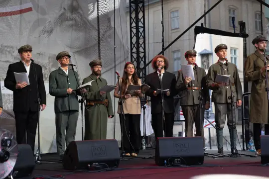 Grupa osób w strojach historycznych śpiewa na scenie podczas wydarzenia kulturalnego.