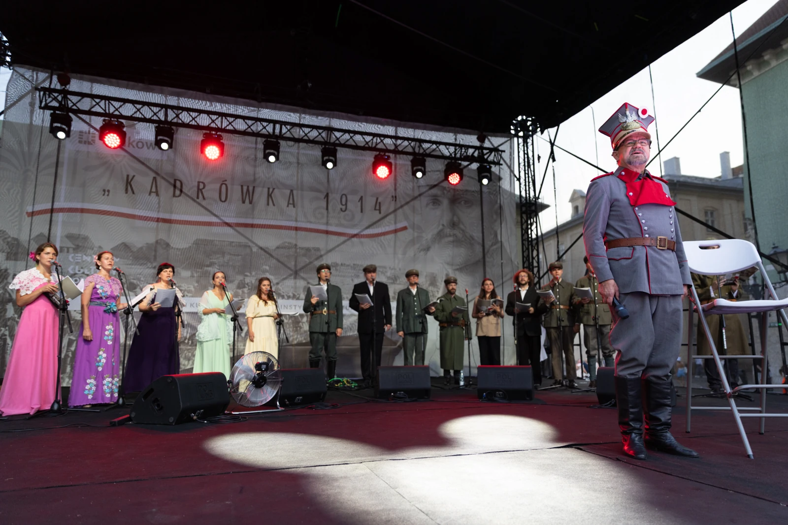 Mężczyzna w mundurze wojskowym na scenie, obok zespół w strojach historycznych.  Autor: Bogusław Świerzowski