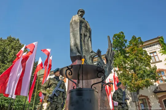 Pomnik z żołnierzem, flagi Polski w tle, uroczystość patriotyczna.