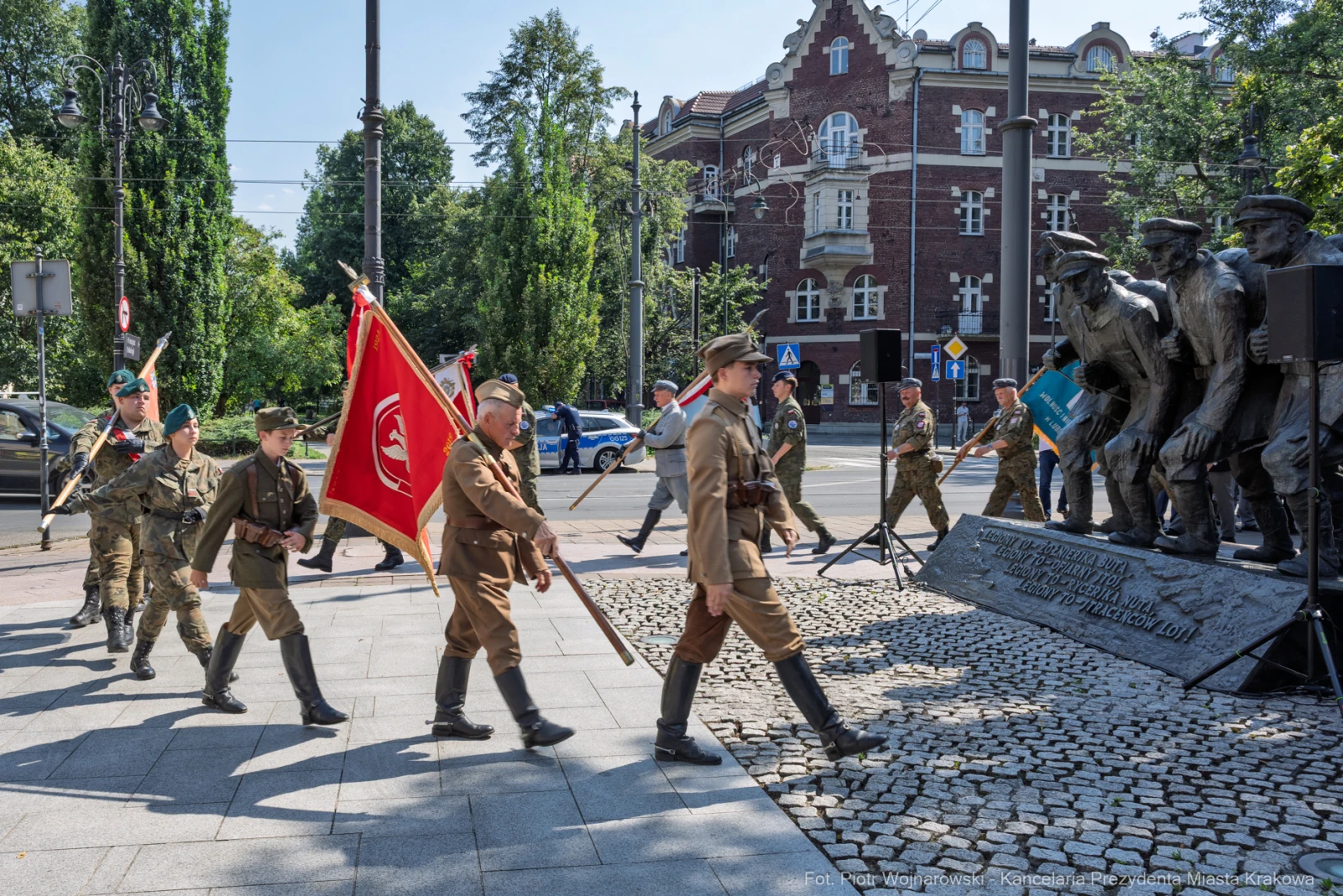 Uczestnicy parady wojskowej z flagami i bronią, obok pomnika.  Autor: Piotr Wojnarowski