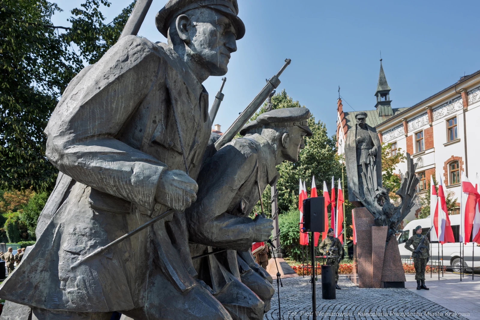 Pomnik żołnierzy z bronią, flagi narodowe w tle, symbolika patriotyczna.  Autor: Piotr Wojnarowski