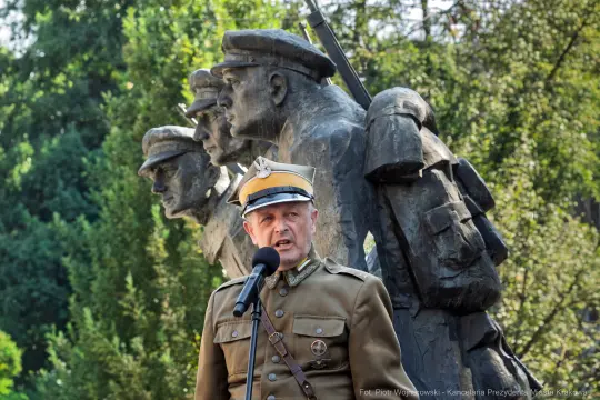 Mężczyzna w mundurze wojskowym przemawia przed pomnikiem żołnierzy.