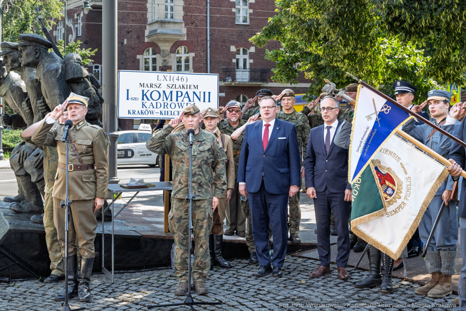 Uroczystość z okazji marszu, uczestnicy w mundurach, flagi i pomnik w tle.  Autor: Piotr Wojnarowski