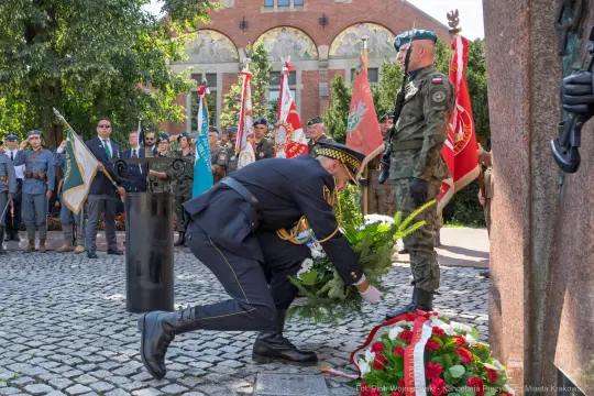 Ceremonia składania wieńców z flagami i żołnierzami w tle.
