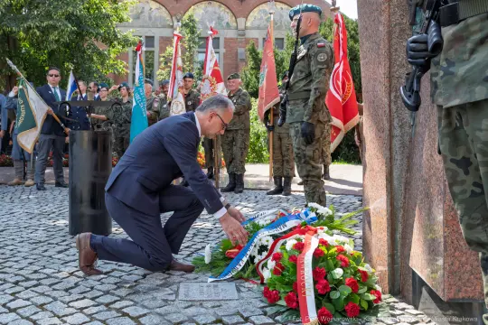 Uroczystość złożenia wieńca w hołdzie poległym, obecność żołnierzy i flagi.