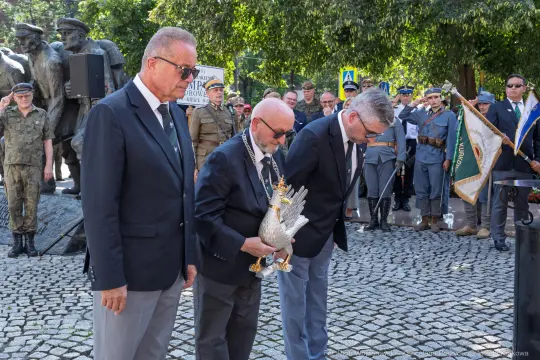 Uroczystość złożenia hołdu z symbolem orła w otoczeniu żołnierzy i uczestników wydarzenia.