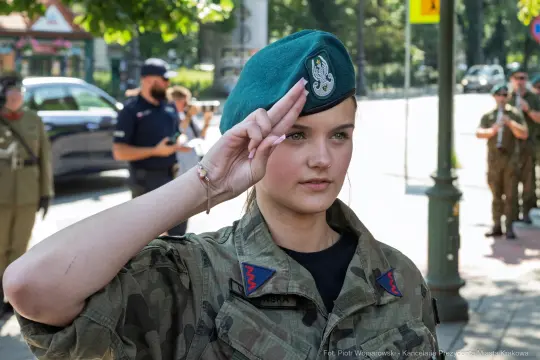 Młoda kobieta w mundurze wojskowym salutuje, nosząc zieloną beretę.