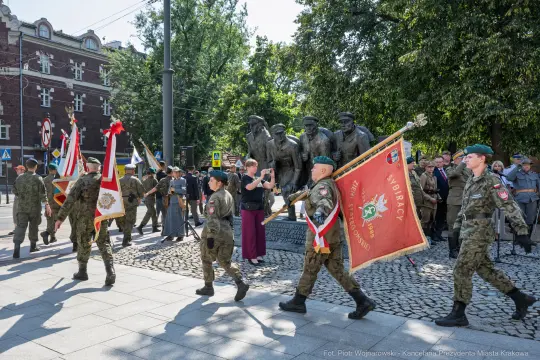 Żołnierze i cywile biorą udział w ceremonii z flagami i sztandarami.