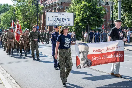 Marsz z flagami i transparentami, uczestnicy w mundurach wojskowych.