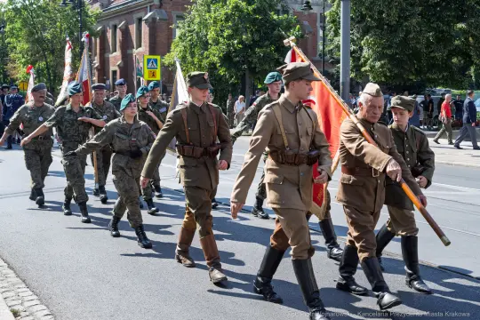 Żołnierze w mundurach historycznych maszerują z flagami podczas parady.