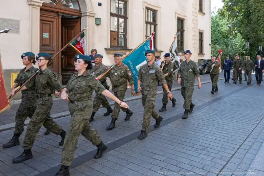 Żołnierze w mundurach maszerują ulicą, niosąc flagi i sztandary.