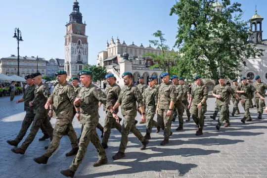 Żołnierze w mundurach maszerują po placu z widokiem na wieżę ratuszową.