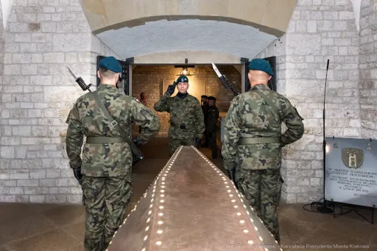 Żołnierze w mundurach salutują w historycznym wnętrzu.